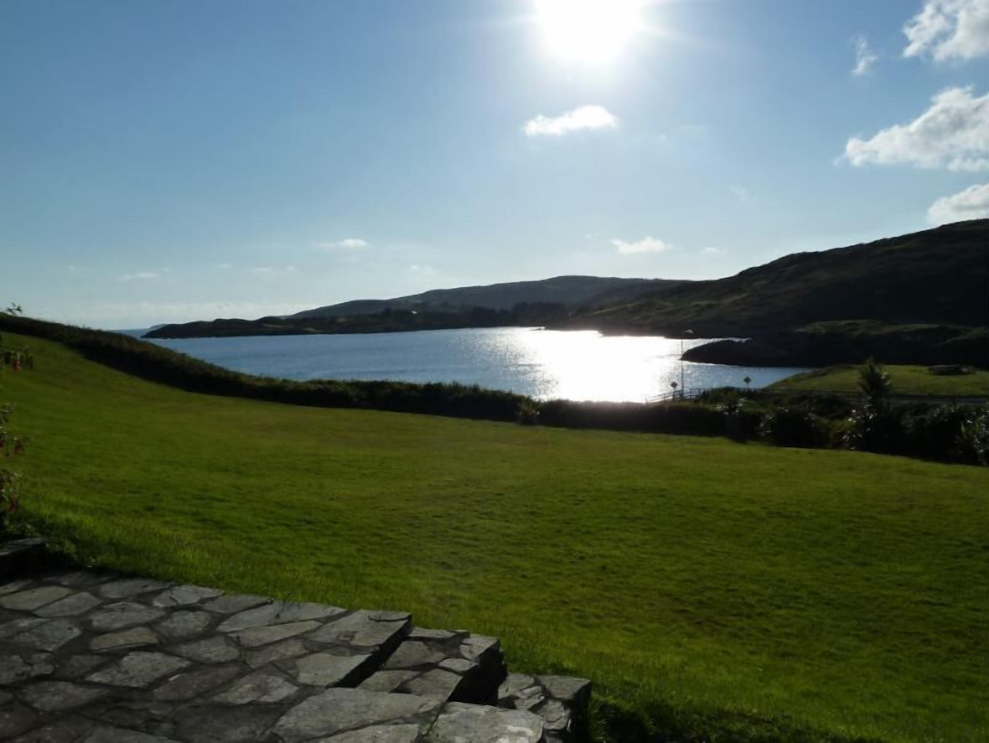 A grassy field with a stone wall in the foreground and a lake in the background.