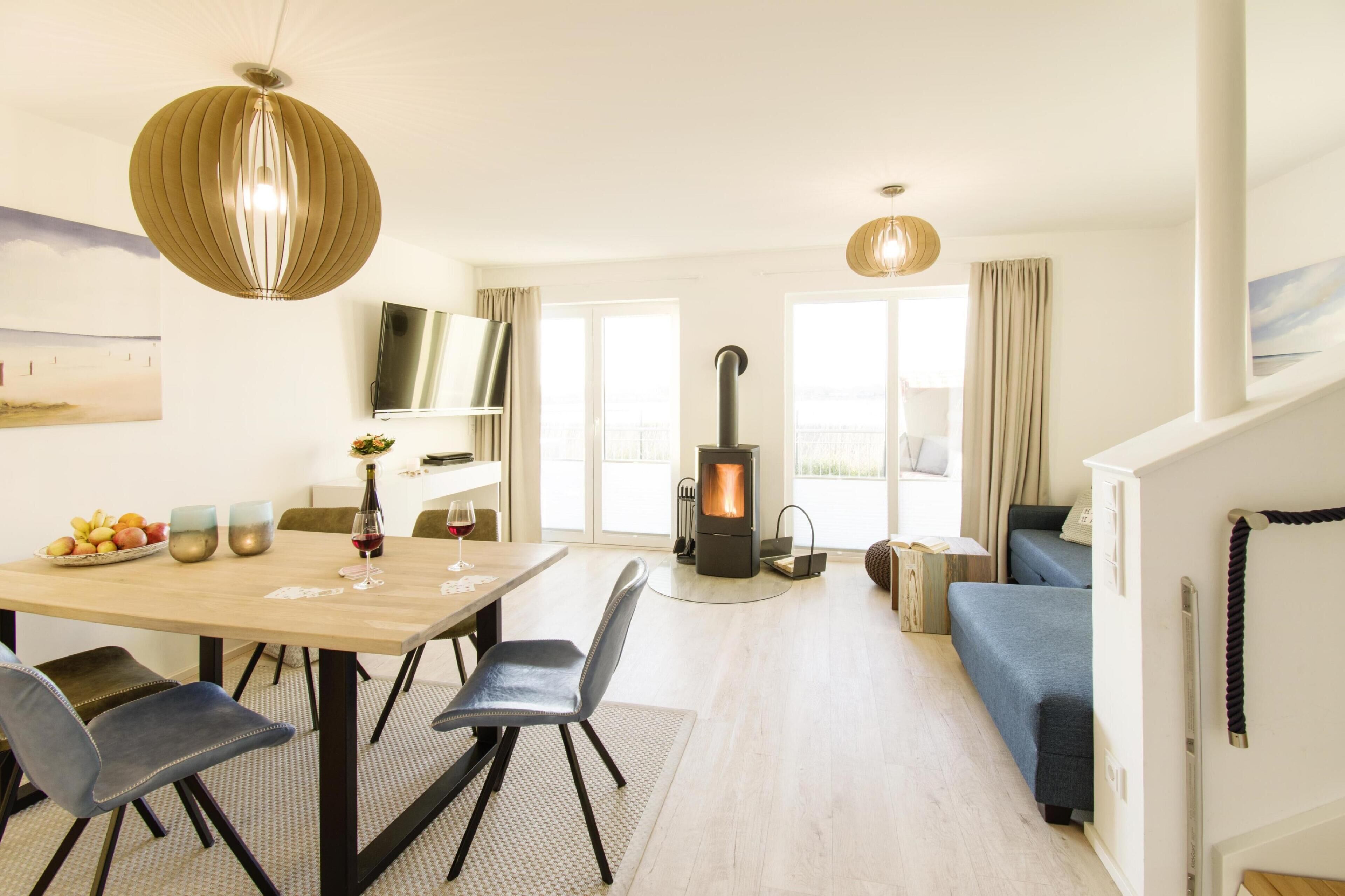 Ein modernes Wohnzimmer mit einem Holzesstisch, Stühlen, einer Couch, einem Kamin und einem Fernseher auf einem Regal.