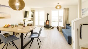 En moderne stue med et træspisebord, stole, en sofa, en pejs og et fjernsyn på en reol.