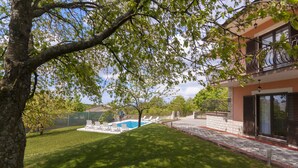 Um imóvel residencial com piscina, um gramado bem cuidado e uma varanda com mobiliário de exterior.