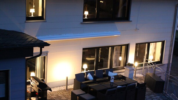 An outdoor patio with a table and chairs, a grill, and a potted plant.
