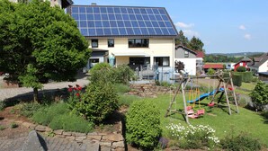 A house with a solar panel roof, a garden with a swing set, and a stone pathway.