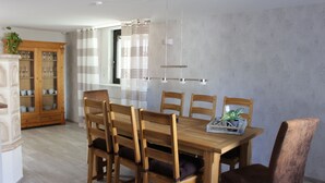 A dining area with a wooden table and chairs, a cabinet with glass doors, and a window with curtains.