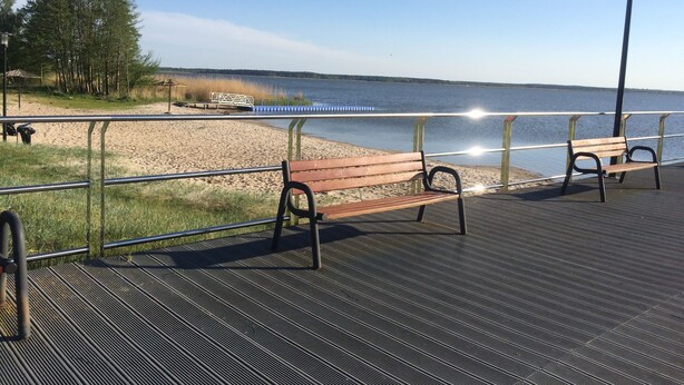Un banco de madera en un paseo marítimo con barandilla, con vista a una masa de agua.