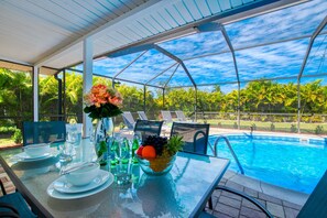 A covered outdoor dining area with a pool view, featuring a table set with plates, bowls, and a fruit bowl. - Beautiful villa in a prime location with large heated pool. (Cape Coral)