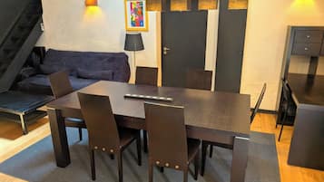 A dining area with a rectangular table, four chairs, a sofa, and a staircase.