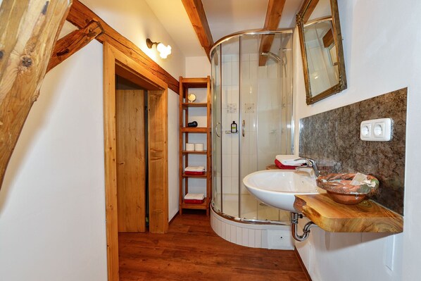A bathroom with a wooden shower enclosure, a sink with a wooden countertop, and a shelf with toiletries.