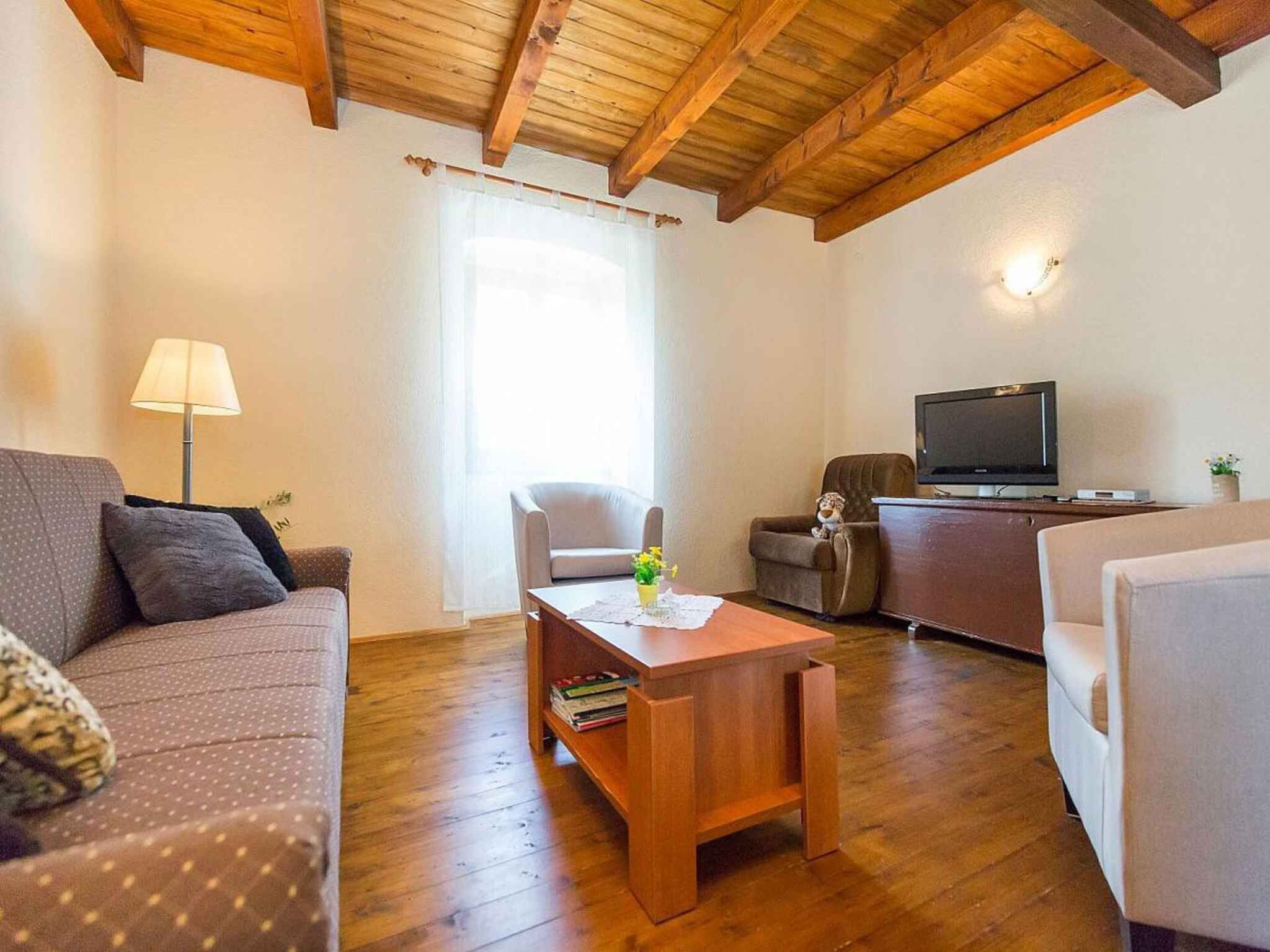 A cozy living room with a wooden ceiling, a sofa, a coffee table, a TV, and a chair.