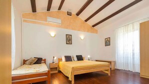 Ein Schlafzimmer mit einem hölzernen Bett, einem zusätzlichen Bett, einem Schreibtisch und einem Stuhl. Es gibt zwei Wandleuchten und einen Deckenventilator.