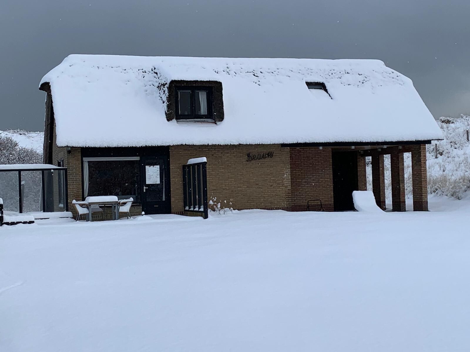 A snow-covered house with a visible door, a window, and a small porch area.