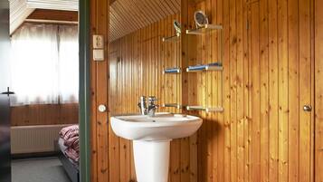 Une salle de bain avec des murs en bois, un lavabo blanc et un miroir.