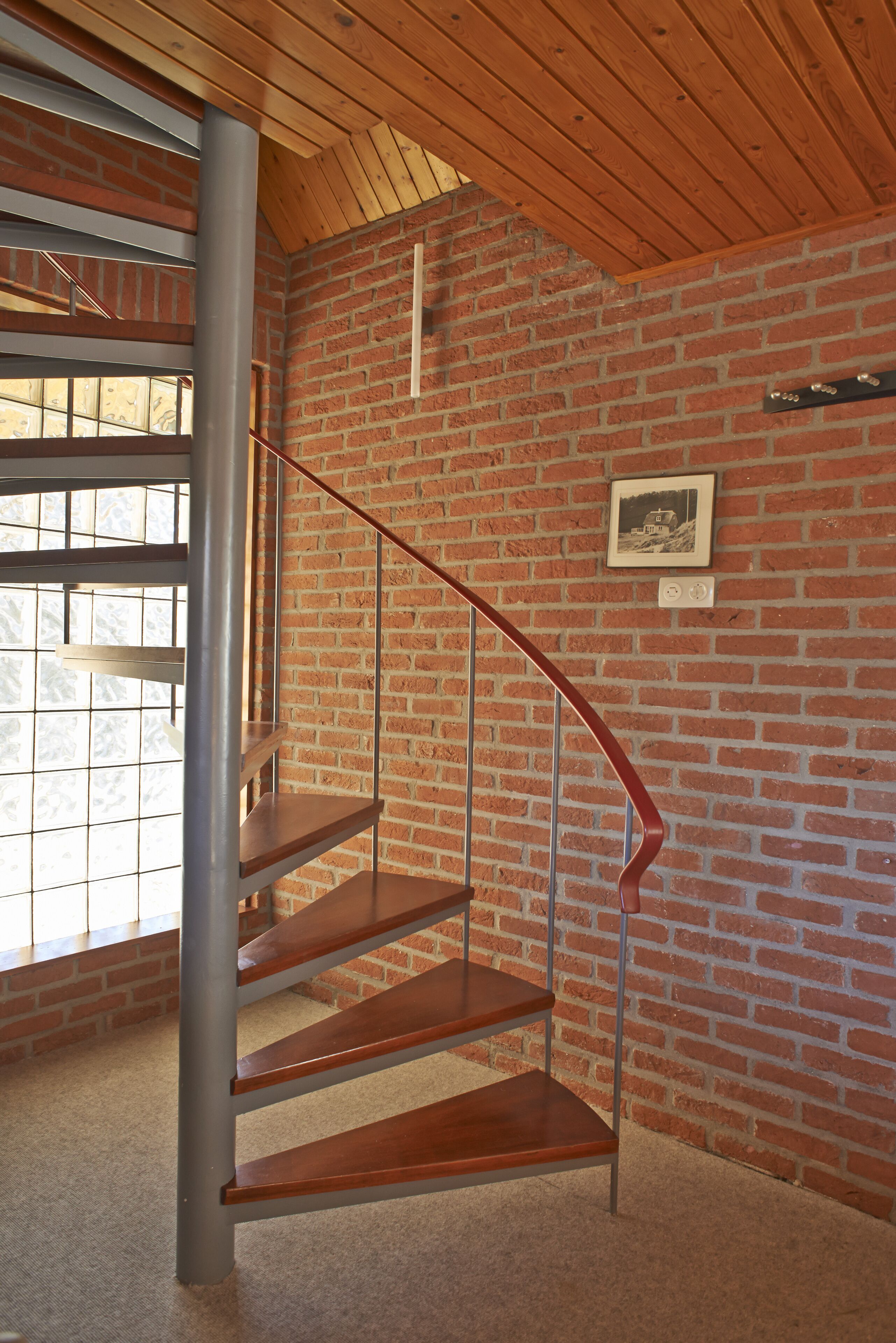 Eine Treppe mit Holzstufen und Metallgeländern in einem Raum mit Ziegelwänden und Holzboden.