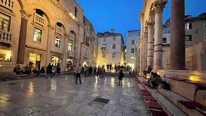 Una piazza storica con edifici in pietra, un'area aperta al centro e gradini che conducono a un livello superiore.