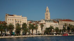 Una passeggiata lungomare con edifici storici, palme e una torre imponente.