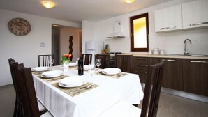 A dining area with a table set for four, a clock on the wall, and a kitchen with modern appliances.
