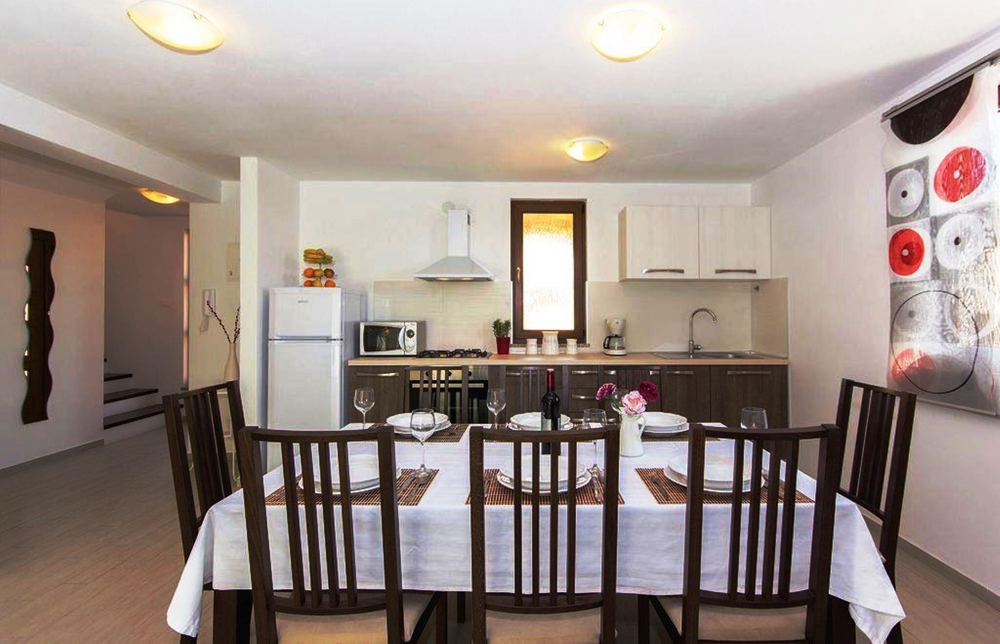 A modern kitchen with white cabinets, a microwave, and a stove. There is a dining table with chairs and a vase of flowers.