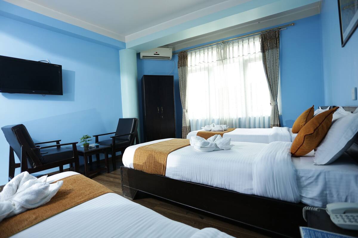 A hotel room with two beds, a desk, a chair, a TV, and an air conditioning unit.