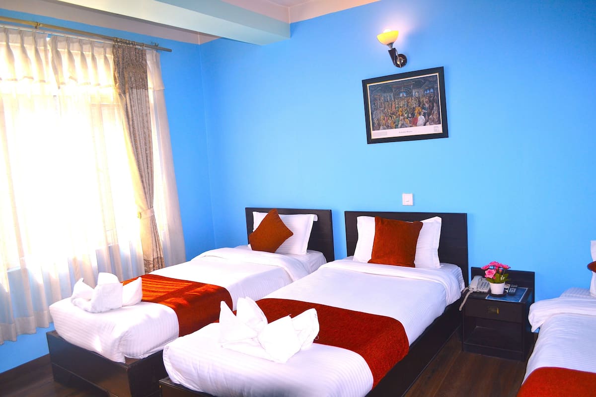 A hotel room with two beds, a nightstand with a phone, a framed picture on the wall, and a window with curtains.