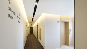 A hotel hallway with numbered rooms on the left, a carpeted floor, and a plain wall on the right. - Brown-dot Hotel Paju Heyri (Paju)