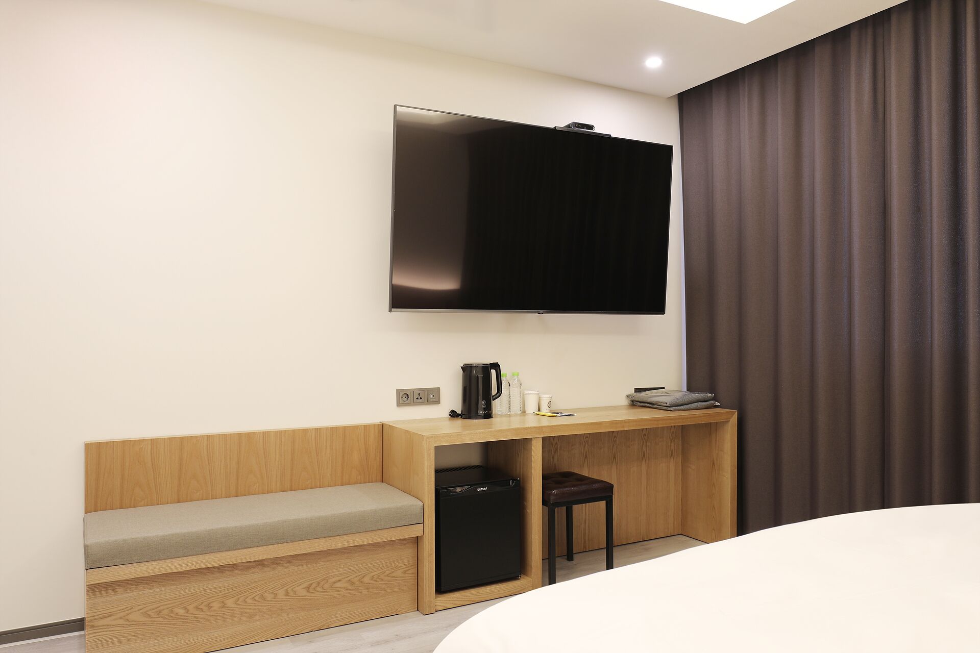 Hotelkamer met een bed, een bureau met stoel, een aan de muur bevestigde televisie en een kleine koelkast.