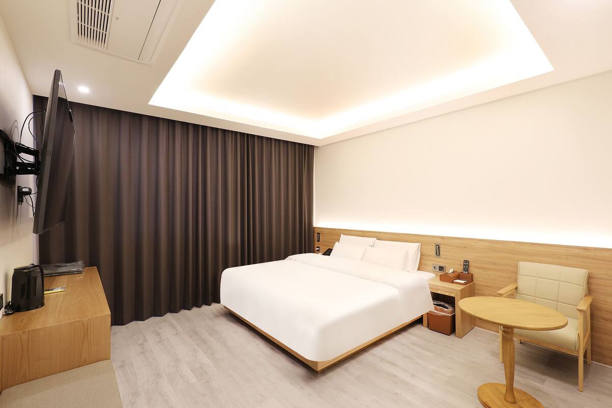 A modern hotel room with a large bed, a bedside table, a small round table, and a TV mounted on the wall.