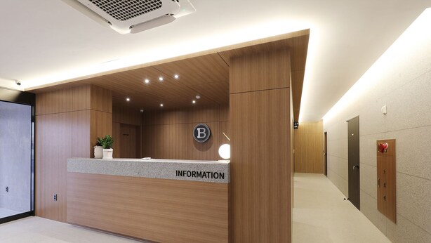 A reception desk with a wooden finish, a sign reading "INFORMATION", and a logo above it. - Brown-dot Hotel Paju Heyri (Paju)