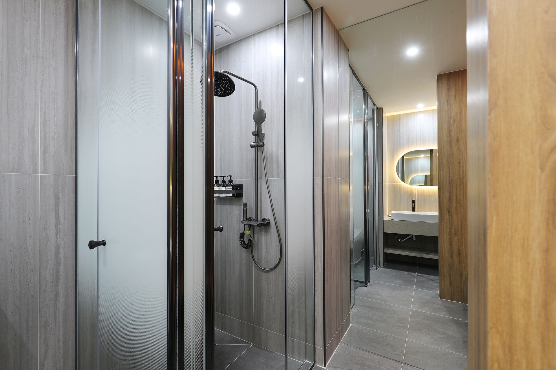 A modern bathroom with a glass-enclosed shower, a wooden vanity, and a mirror with built-in lighting.