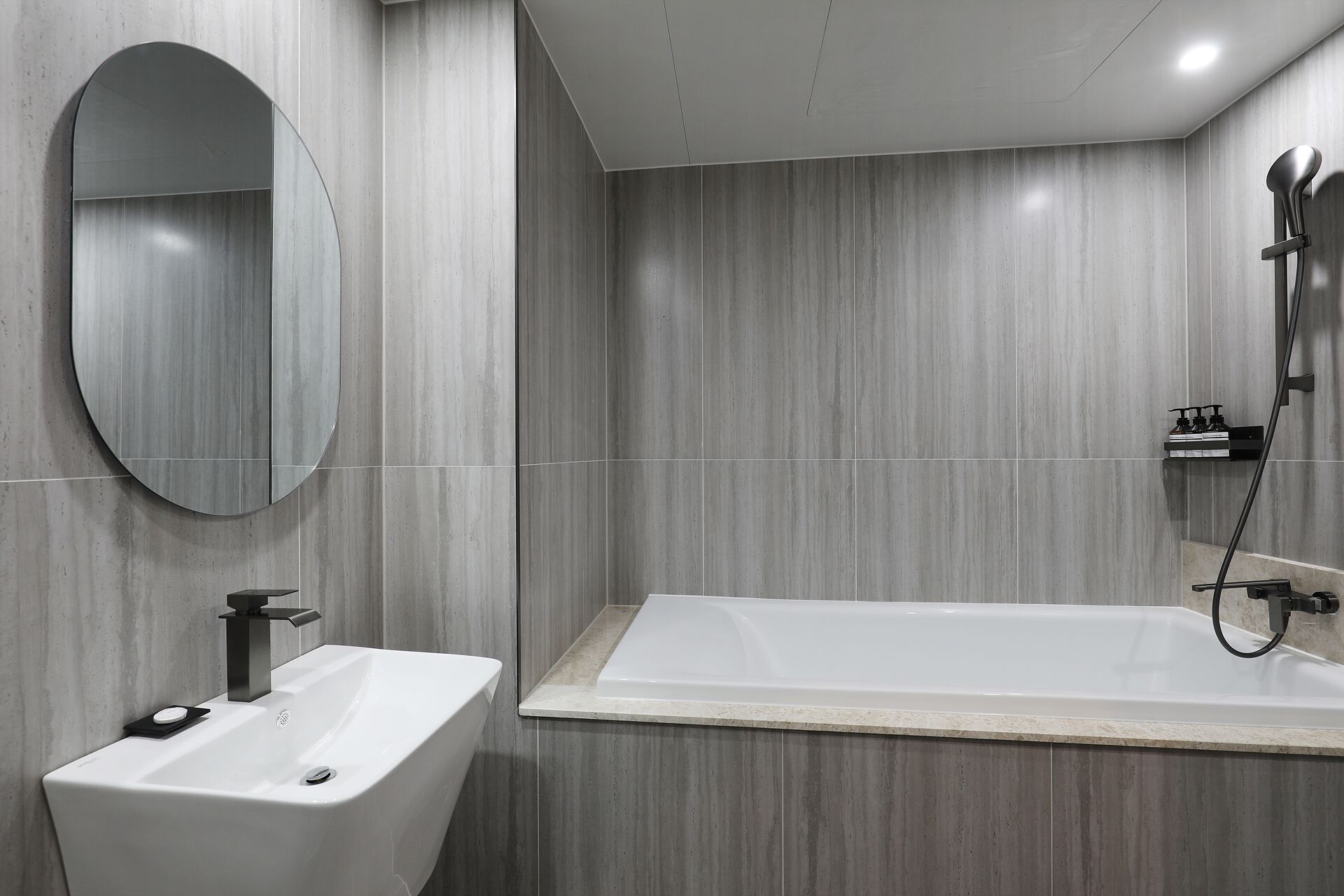 A modern bathroom with a rectangular bathtub, a round mirror, and a white sink.