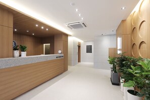 Un área de recepción moderna con un mostrador de madera, un panel informativo digital y plantas en macetas.