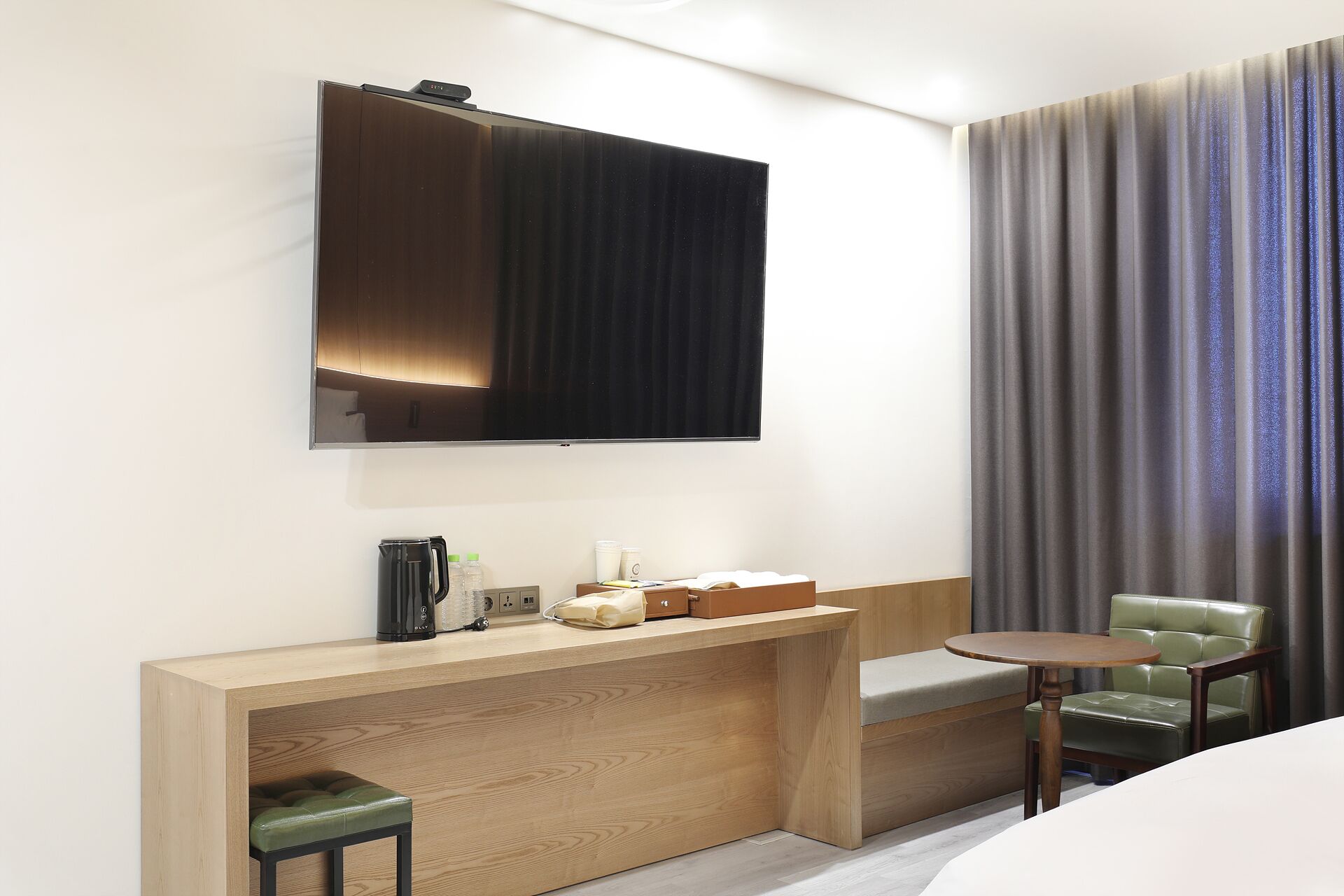 Habitación de hotel con un escritorio de madera, un televisor de pantalla plana, una silla verde y una mesita.