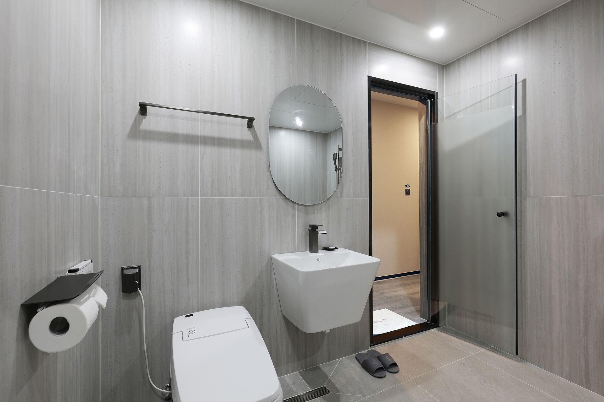 A modern bathroom with a toilet, sink, mirror, and shower.