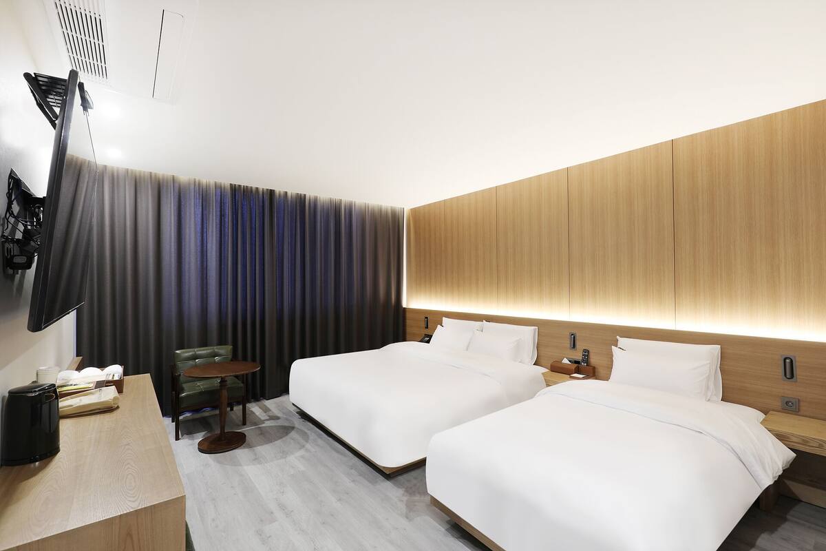 A hotel room with two beds, a desk, a chair, a TV, and a curtain.
