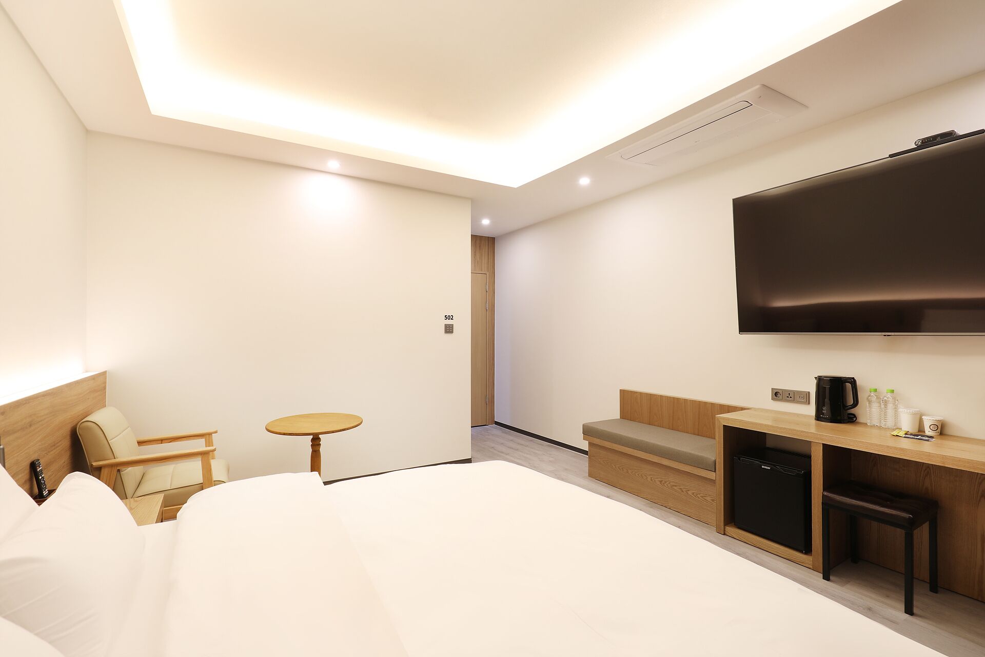 A modern hotel room with a large bed, a desk with a flat-screen TV, a small table, and a sofa.