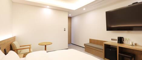 A modern hotel room with a large bed, a desk with a flat-screen TV, a small table, and a sofa.