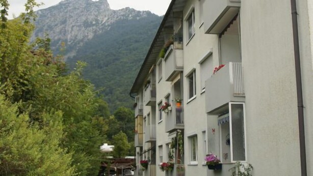 A multi-story building with balconies, a grassy courtyard, and a mountainous backdrop. - Cozy city apartment with carport for 2 to 5 people near the thermal baths (Bad Reichenhall)