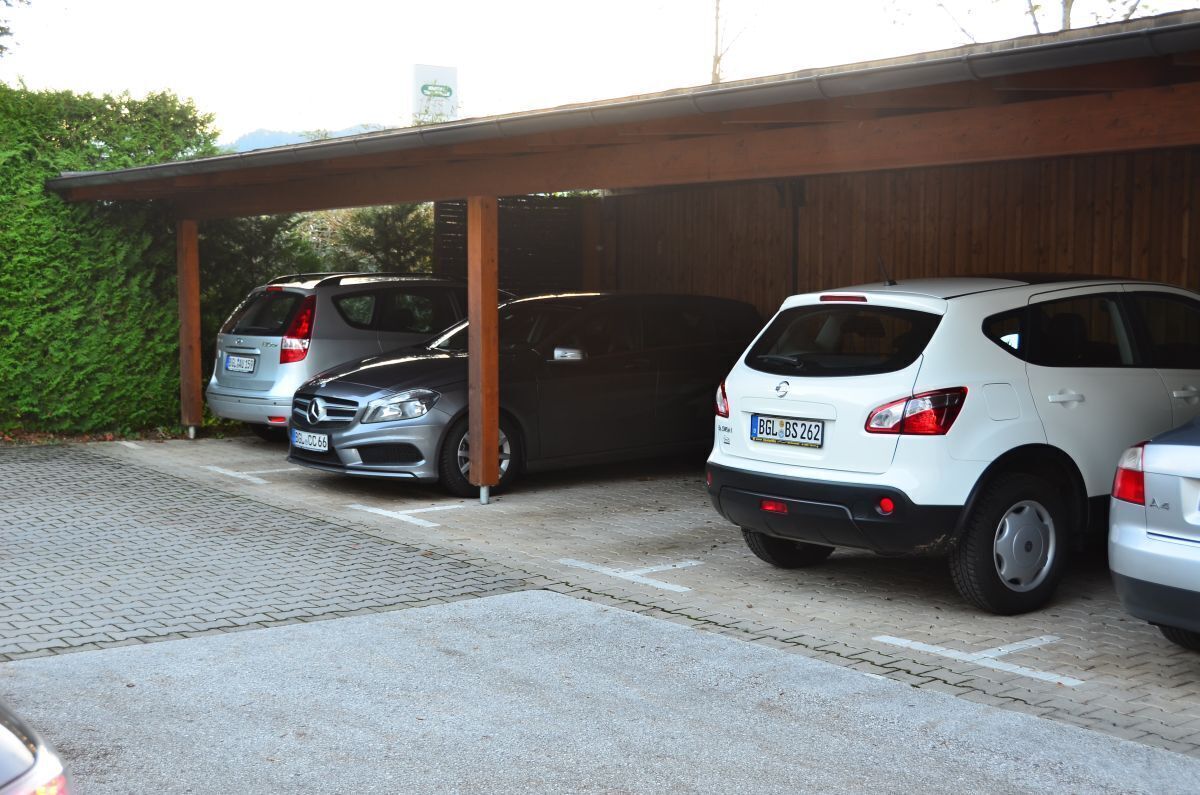 A covered parking area with three cars parked under a wooden structure.
