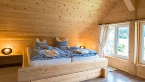 A wooden cabin bedroom with a bed, bedside lamps, and a window with curtains.