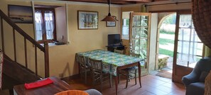 Una sala de estar acogedora con una escalera de madera, un comedor con mesa y sillas, un televisor y un ventanal con vistas al exterior.
