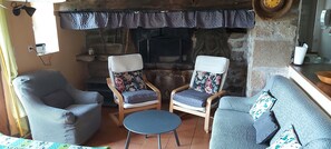 Un salón acogedor con dos sillones, un sofá y una mesita. Un rincón con chimenea de piedra al fondo.