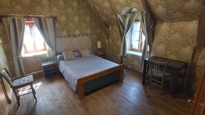 A bedroom with a wooden bed, a bedside table, a chair, and a window with curtains.