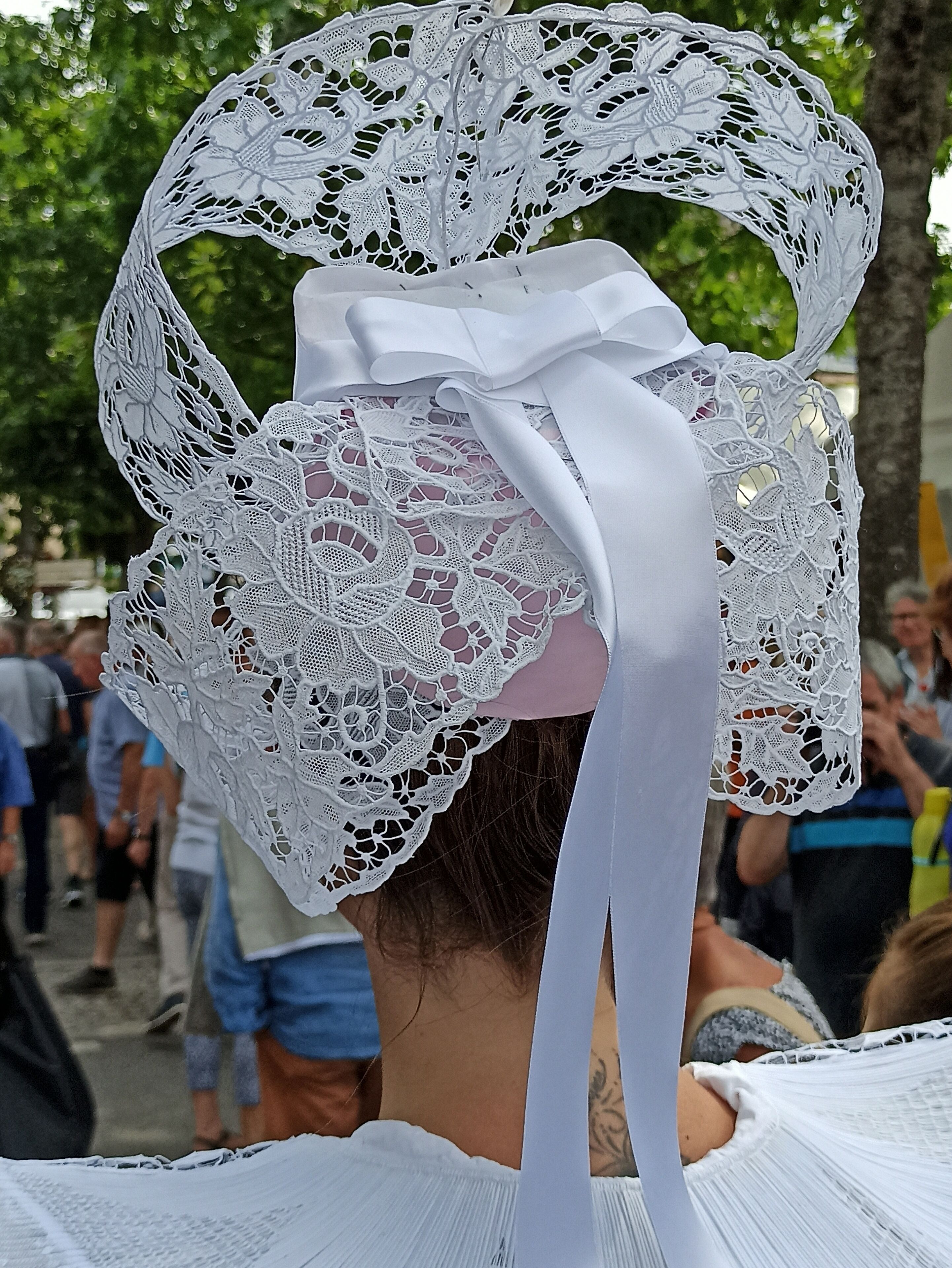A person wearing a white lace headpiece with a ribbon.