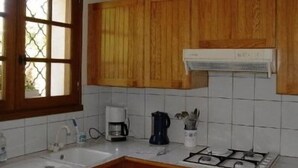 Une cuisine avec des meubles de rangement en bois, une cuisinière à gaz, une machine à café et une fenêtre ornée d’une grille décorative.