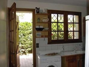 A compact kitchen with a washing machine, a sink, and a window with a view of greenery.