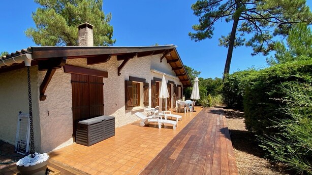 Un chalet rustique doté d’une terrasse en bois, d’un espace salon extérieur et d’une cheminée en pierre.