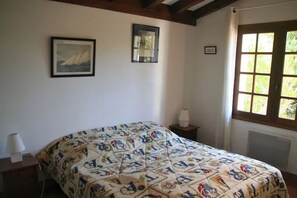 A bedroom with a bed, two framed pictures on the wall, a nightstand with a lamp, and a window with curtains.