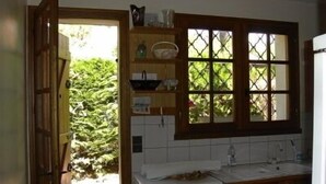 Une cuisine équipée d’un lave-linge, une fenêtre à carreaux et une porte donnant sur un jardin.