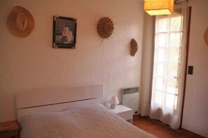 Un dormitorio con cama, mesita de noche, lámpara y ventana con cortinas.