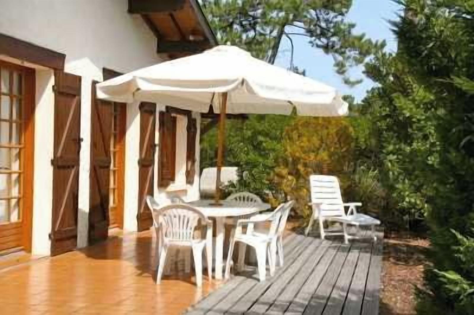 Une terrasse extérieure avec une table et des chaises, un parasol blanc et une plateforme en bois.