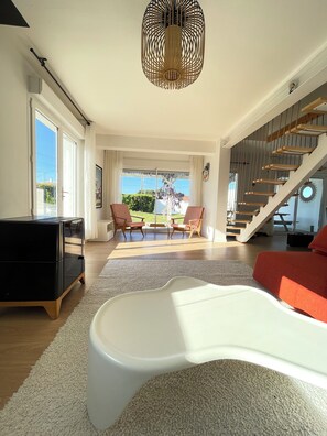 A modern living room with a sofa, chairs, a TV, and a staircase. - Old Boucau les Bains Villa  (Vieux-Boucau-Les-Bains)
