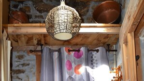 A rustic room with a wooden chair, a hanging light fixture, and a curtain with a circular pattern. - CHARMING HOUSE ON THE EDGE OF CEVENNES NATIONAL PARK (Meyrueis)